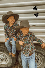 Load image into Gallery viewer, Two boys dressed in western attire. One is sitting on the edge of a trailer, and the other is standing up leaning against it. They are both smiling, looking off to the side.