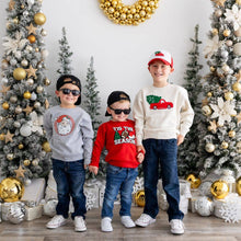 Load image into Gallery viewer, Three young boys dressed in Christmas-themed outfits standing in front of a festive holiday display with decorated trees and gold ornaments. The boys wear sweaters featuring holiday designs: a gray Santa cat, a red 'Tis the Season' football sweater, and a cream sweater with a red truck and Christmas tree design. Casual holiday style for kids.