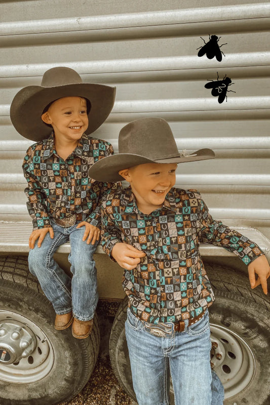 Two boys dressed in western attire. One is sitting on the edge of a trailer, and the other is standing up leaning against it. They are both smiling, looking off to the side.