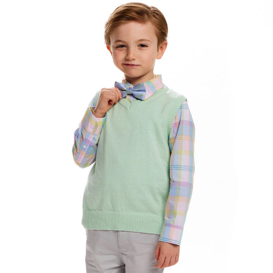 A smirking male child with strawberry blonde hair is wearing a pastel-colored outfit, including a blue and green plaid Bow-tie, a pink plaid button up shirt, and a pastel green sweater vest. He is also wearing light grey chinos.