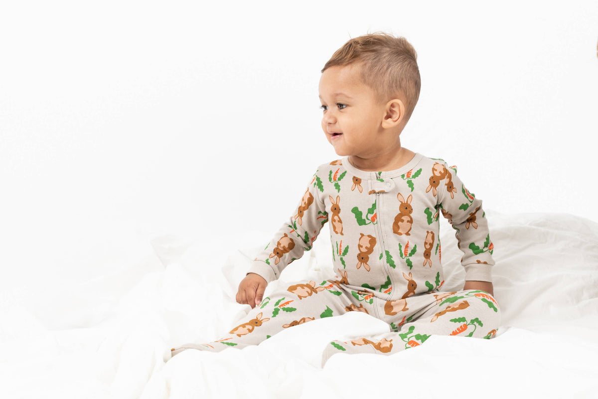 Happy baby wearing Easter bunny-themed footie pajama romper for toddlers with carrots and green leaves print — soft cotton baby sleepwear outfit