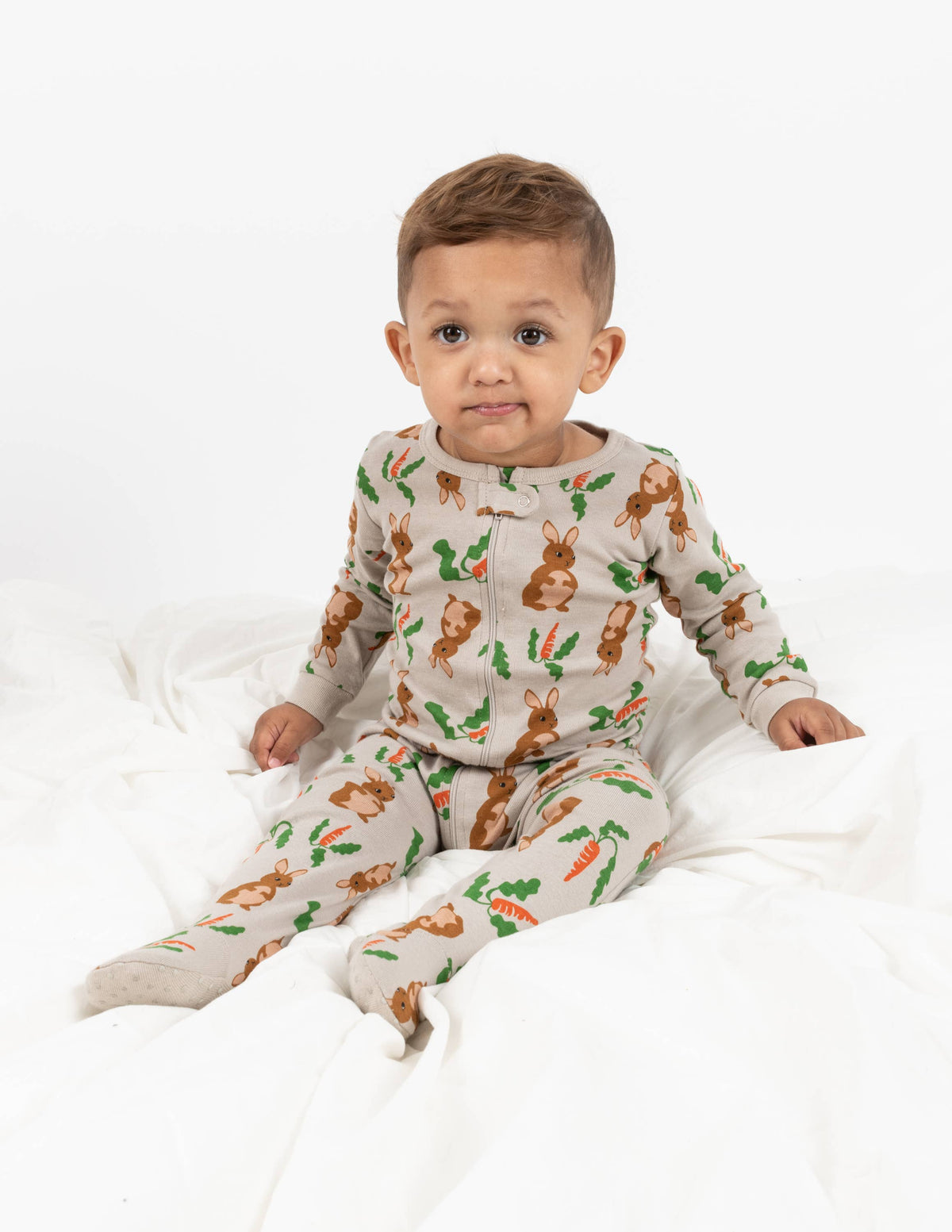 Smirking baby wearing Easter bunny-themed footie pajama romper for toddlers with carrots and green leaves print — soft cotton baby sleepwear outfit