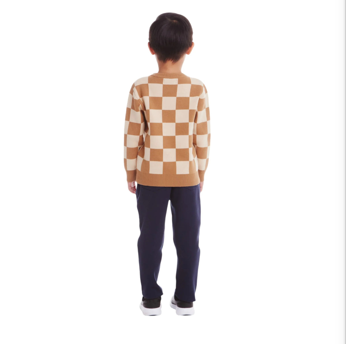 Young boy wearing a tan and beige checkered sweater. His back is facing the camera.  He is wearing navy pants and black shoes. 