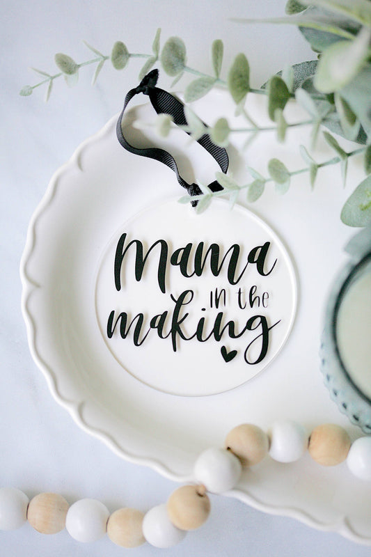 Clear acrylic Mama In The Making ornament with vinyl detail, 4 inch diameter, black ribbon hanger