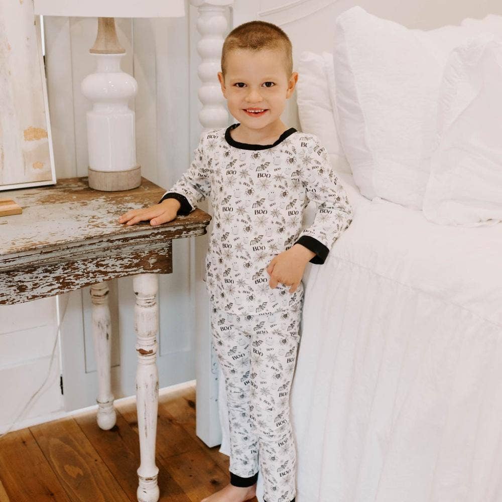 White pajamas with black trim and Halloween print featuring bats, spiders, and webs